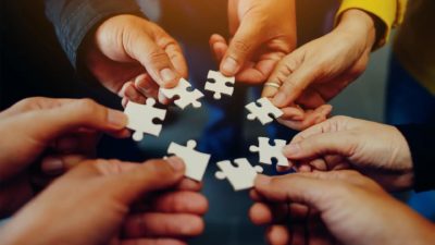 7 Hände halten Puzzelstücke im Kreis aneinander